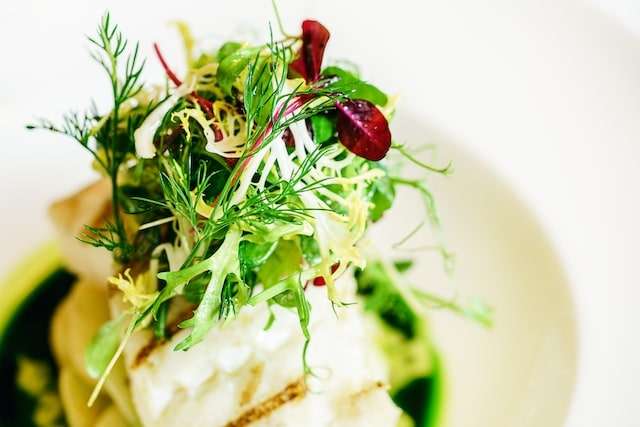 grilled cod loin on a bed of potato served with parsley sauce and micro herbs and salad leaves